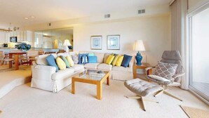 A modern living room with a sofa set, a coffee table, and a chair. There is a dining area in the background with a table and chairs. - Seaside Villas oceanfront townhome with 2 balconies, beach access & sunrise view (Fenwick Island)