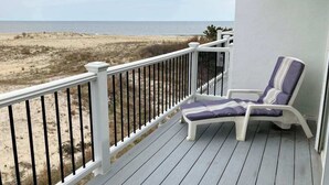 A balcony with a white railing, a single lounge chair with a cushion, and a view of a beach and ocean. - Seaside Villas oceanfront townhome with 2 balconies, beach access & sunrise view (Fenwick Island)