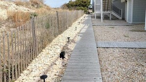 A wooden deck leading to a house with a garage, surrounded by a wooden fence and a gravel path. - Seaside Villas oceanfront townhome with 2 balconies, beach access & sunrise view (Fenwick Island)