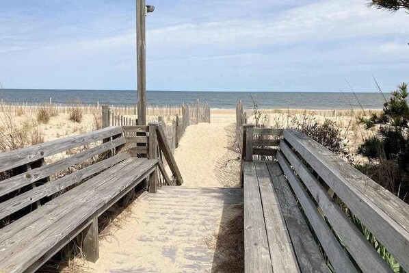 A wooden boardwalk leading to a sandy beach with a wooden fence on either side.