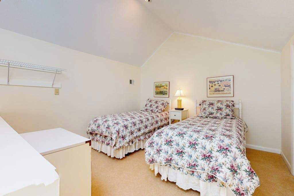 Une chambre avec deux lits, une table de chevet, une lampe et une étagère fixée au mur.