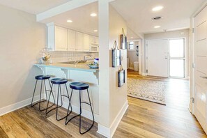 A kitchen with white cabinets, a bar stool area, and a wooden floor. - Stunning beachfront condo with pool, sauna, balcony, W/D (Bethany Beach)