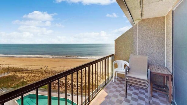 Un balcone con vista sulla spiaggia e sull'oceano, una piscina e un'area salotto esterna.
