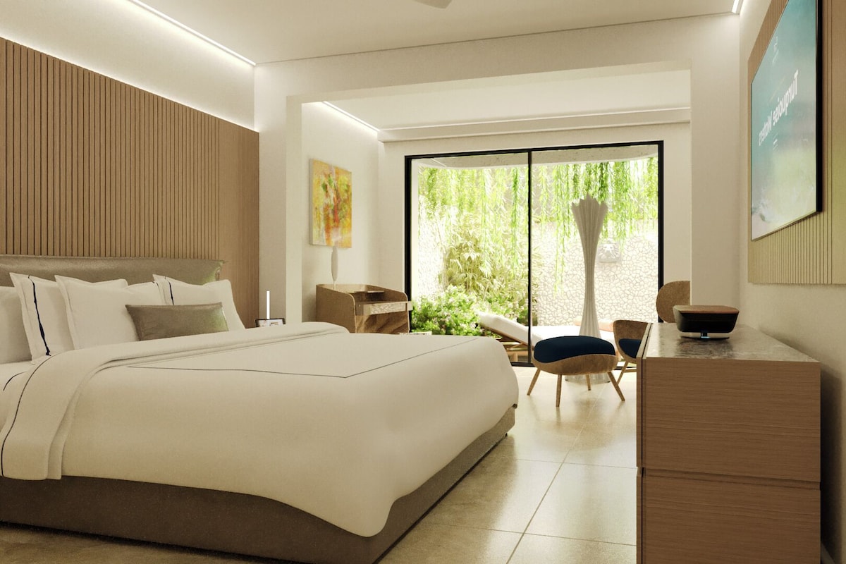A modern hotel room with a large bed, a desk, and a view of greenery through the window.