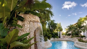 A pool with a waterfall, surrounded by tropical plants and a stone wall.