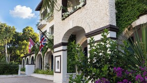 A building with arched windows, a flag, and a garden with purple flowers.
