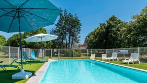 A swimming pool with lounge chairs and umbrellas, surrounded by a fence and trees. - Gîte Le Grand Chêne: Shared Pool, Wi-Fi & Air Conditioning in Lesperon (Lesperon)