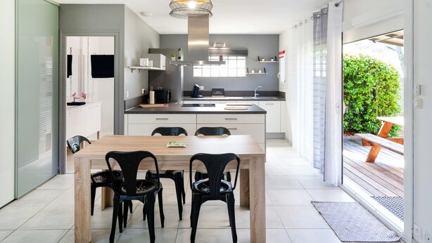 A modern kitchen with a central island, black chairs, and a wooden dining table. - Gîte Le Grand Chêne: Shared Pool, Wi-Fi & Air Conditioning in Lesperon (Lesperon)