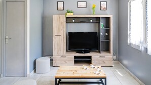 A modern living room with a flat-screen TV, wooden entertainment unit, and a coffee table. - Gîte Le Grand Chêne: Shared Pool, Wi-Fi & Air Conditioning in Lesperon (Lesperon)