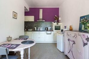 A compact kitchen with white cabinets, a purple wall, a microwave, a kettle, and a dining table with chairs.