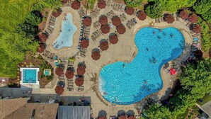Luftaufnahme eines Resorts mit mehreren Schwimmbecken, Liegestühlen und Sonnenschirmen.