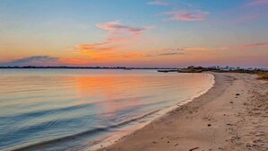 Ein Strand mit ruhiger See, sandigem Ufer und einer fernen Stadtansicht.
