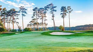 Ein Golfplatz mit Sandbunkern, Bäumen und blauem Himmel.