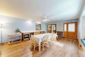 Uma sala de jantar com mesa e cadeiras, um ventilador de teto e piso de madeira.