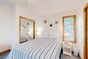Quarto com cama, mesas de cabeceira, espelho e janela com persianas.