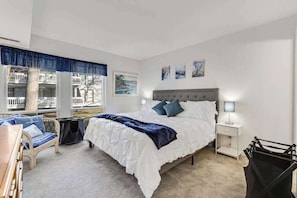 A bedroom with a bed, bedside tables, a chair, a window with a view, and artwork on the wall. - Sea Colony condo with indoor/outdoor pools, sports courts, & beach access (Bethany Beach)