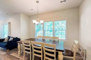 A dining area with a wooden table and chairs, a chandelier, and large windows with a view of greenery. - Seashore Villas townhouse w/patio, grill & shared community pool (Selbyville)