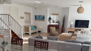 A spacious living area with a glass dining table, sofas, a TV, and a staircase.