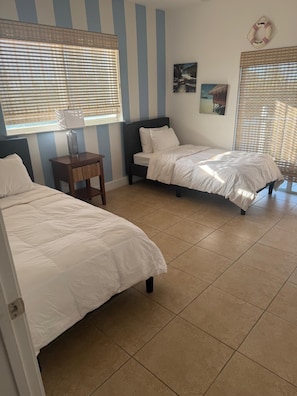 Una habitación con dos camas, una mesita de noche con lámpara, paredes a rayas y un adorno con flotador de salvamento.