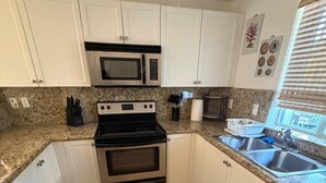A kitchen with white cabinets, a microwave, a stove, and a sink.