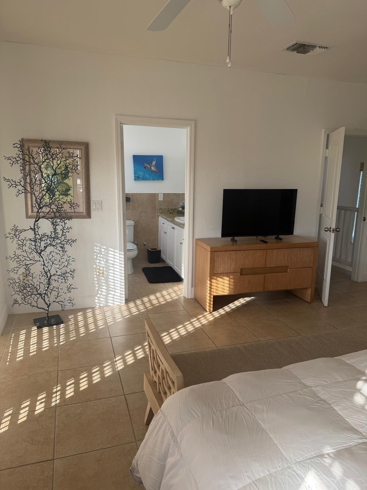 Un dormitorio con cama, televisor, cómoda de madera, un cuadro enmarcado y una pequeña escultura de árbol.