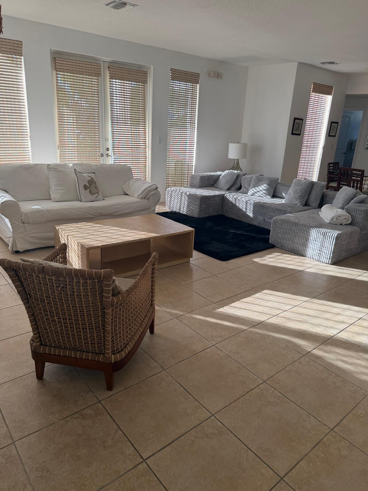 Un salon avec un canapé blanc, un fauteuil en osier, une table basse et un canapé à rayures.