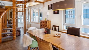 A wooden staircase, a dining table with chairs, and a view of the outside through large windows.