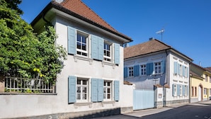 A two-story building with blue shutters, a tiled roof, and a visible chimney.