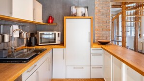 A modern kitchen with white cabinets, a wooden countertop, a microwave, a kettle, and a sink.
