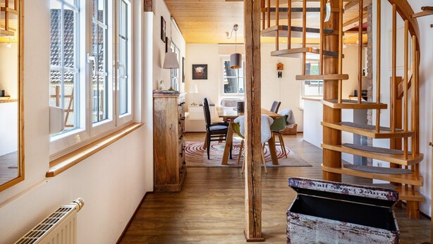 A wooden staircase leading to a loft bedroom with a view of the outdoors.