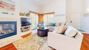 Een moderne woonkamer met een open haard, een televisie, een grote bank en een bordje met de tekst 'BETHANY BEACH'.