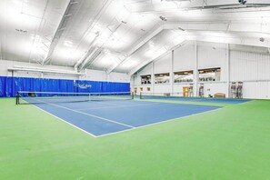 An indoor tennis court with a net, blue and green flooring, and a high ceiling with visible structural beams. - Sea Colony condo with multiple pools, sports courts & beach access (Bethany Beach)