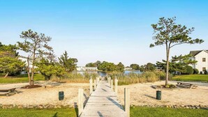 Une promenade en bois mène à une plage bordée d’arbres, avec une étendue d’eau en arrière-plan.