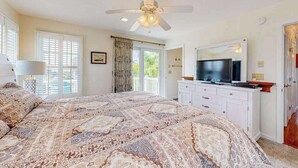 Une chambre à coucher avec un grand lit, un ventilateur de plafond, une télévision et une fenêtre avec des rideaux.