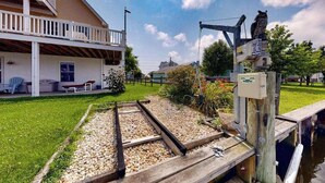 Une maison avec un balcon, un jardin avec un chemin de gravier et une jetée qui s’avance dans l’eau.