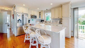 Une cuisine moderne avec des meubles blancs, un îlot central doté de tabourets, un four encastré et une grande fenêtre.