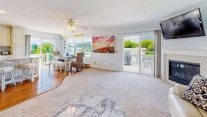 Un salon spacieux doté d’une cheminée, d’un téléviseur fixé au mur et d’un balcon aménagé avec du mobilier d’extérieur.