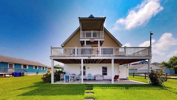 Une maison à deux étages avec un balcon, une terrasse couverte et une pelouse.