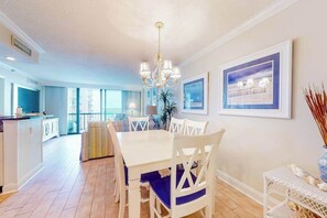 A dining area with a white table and chairs, a chandelier, and framed artwork on the walls. - Sea Colony beachfront 6th-floor condo with 12 pools, 2 hot tubs, private beach (Bethany Beach)
