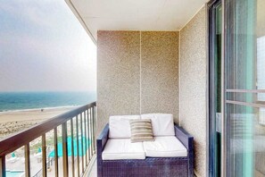 A balcony with a wicker sofa, a striped pillow, and a view of the beach and ocean. - Sea Colony beachfront 6th-floor condo with 12 pools, 2 hot tubs, private beach (Bethany Beach)