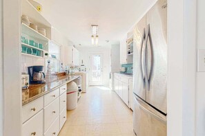 A narrow kitchen with white cabinets, a stainless steel refrigerator, and a coffee maker on the counter. - South Bethany home - just steps to the beach! With screened deck, AC & W/D (Bethany Beach)