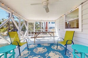 A covered porch with two chairs, a table, and a ceiling fan. - South Bethany home - just steps to the beach! With screened deck, AC & W/D (Bethany Beach)