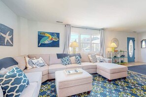 A living room with a sofa, ottoman, and a patterned rug. - South Bethany home - just steps to the beach! With screened deck, AC & W/D (Bethany Beach)