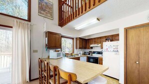 A kitchen with wooden cabinets, a central island with chairs, a microwave, and a refrigerator. - Secluded, 4-BR, dog-friendly home, private beach (Bethany Beach)