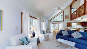 A spacious living room with a white sofa, blue sofa, and a coffee table. There is a dining area with a table and chairs, and a kitchen area visible in the background. - Secluded, 4-BR, dog-friendly home, private beach (Bethany Beach)
