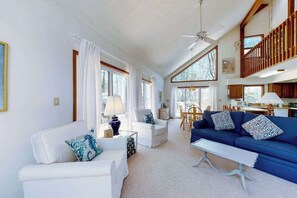 A spacious living room with a white sofa, blue sofa, and a coffee table. There is a dining area with a table and chairs, and a kitchen area visible in the background. - Secluded, 4-BR, dog-friendly home, private beach (Bethany Beach)