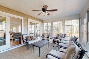 Ein Wintergarten mit Deckenventilator, großen Fenstern und einer Sitzecke mit Sofas und Sesseln.