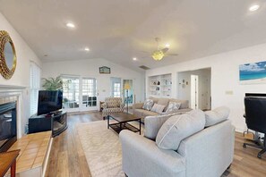 Ein geräumiges Wohnzimmer mit Kamin, Fernseher, Sofa und Deckenventilator.