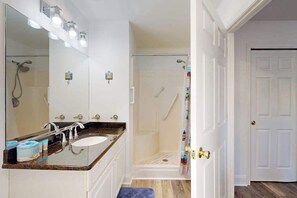 Un bany amb un mirall gran, un lavabo, una dutxa i una porta.