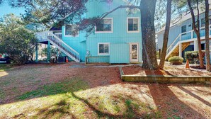 Ein zweistöckiges Haus mit blauer Fassade, einer Holztreppe und einem gepflegten Garten mit Bäumen und einem kleinen Gemüsegarten.